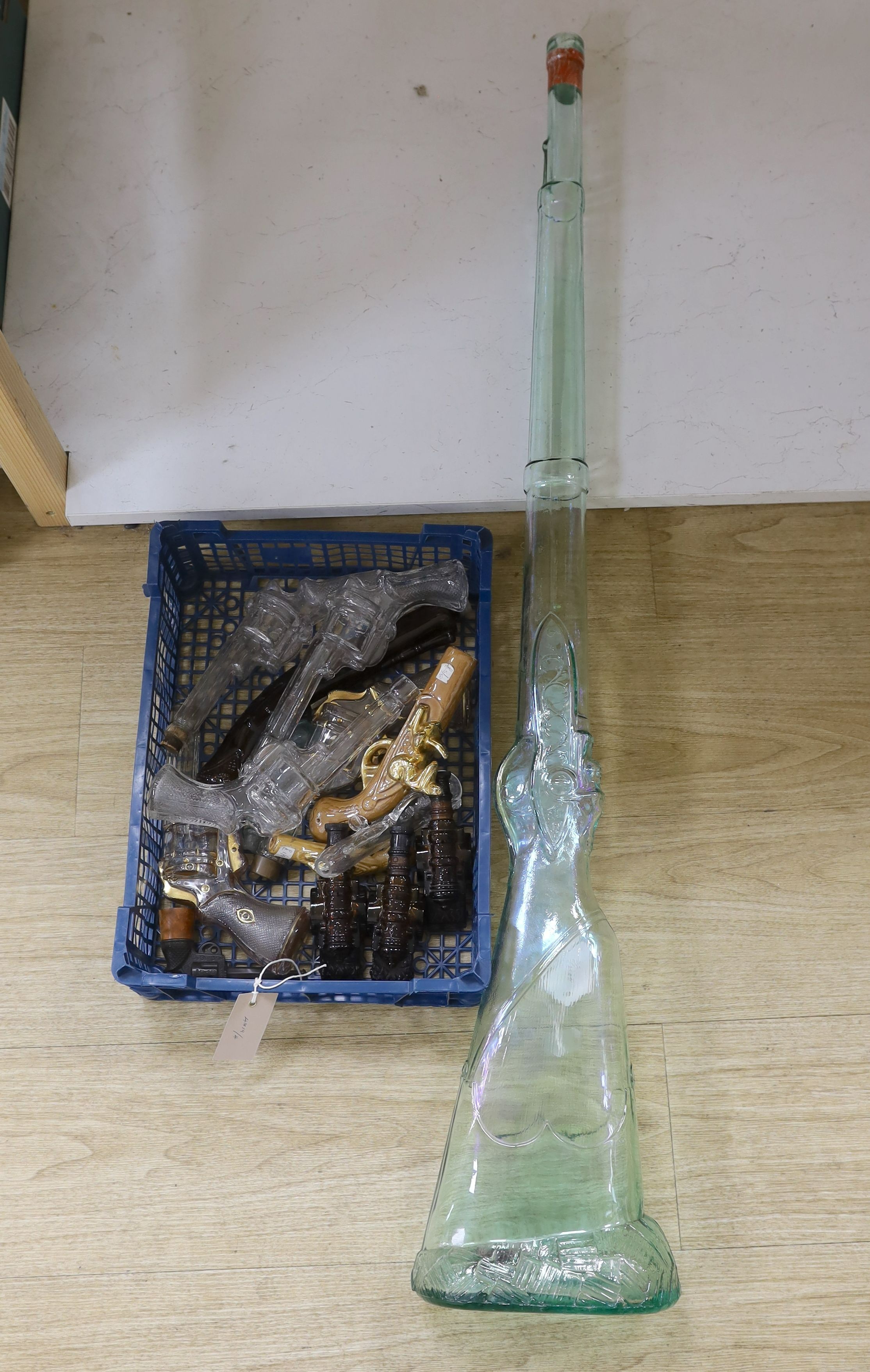 A novelty pressed bottle-green glass rifle and a collection of novelty glass pistols and cannon, Rifle 105 cms high.